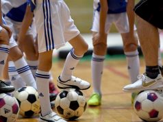What are the reasons for playing various sports? A group of people standing next to a football ball